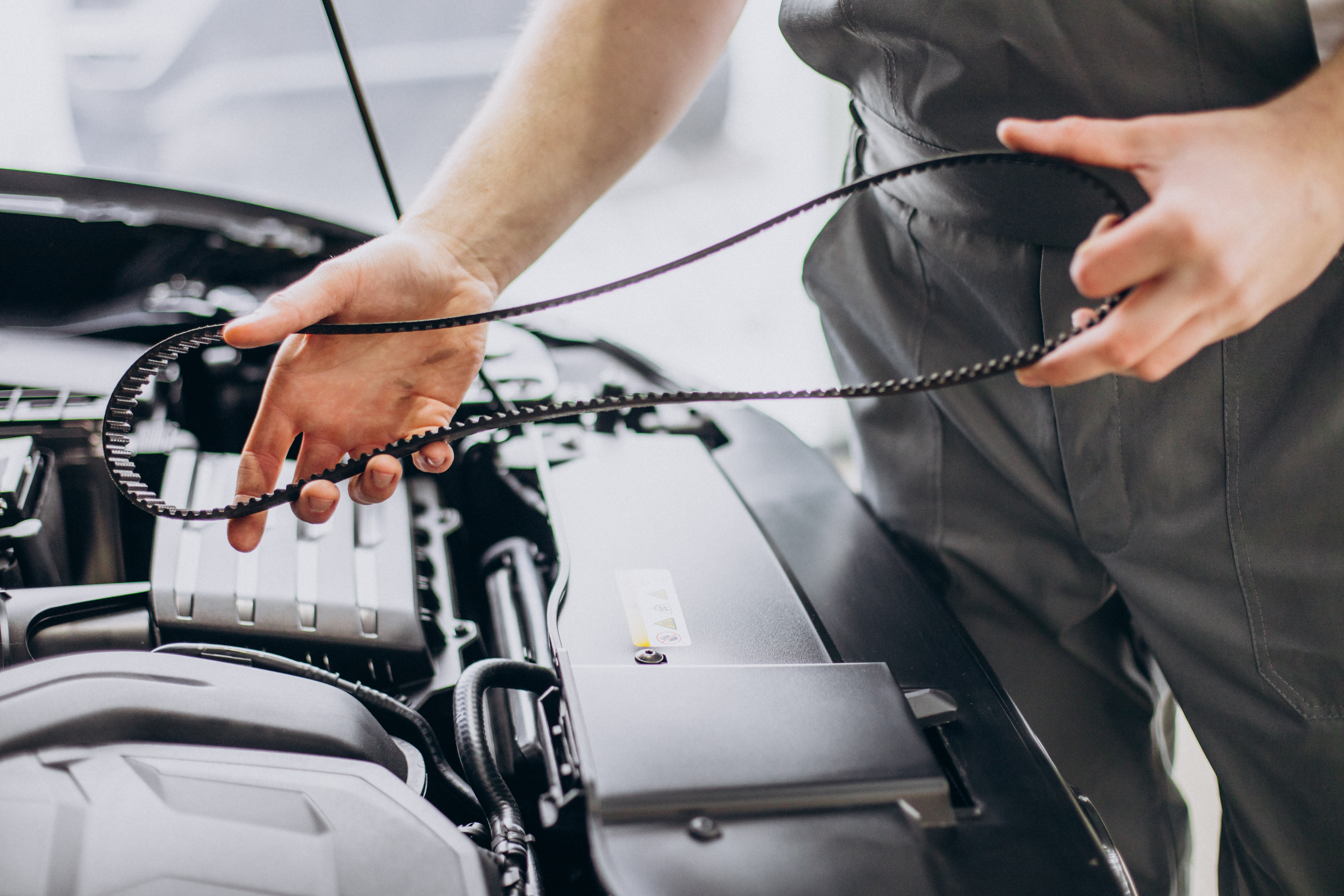Close-up of a mechanic holding a replacement timing belt by a car engine